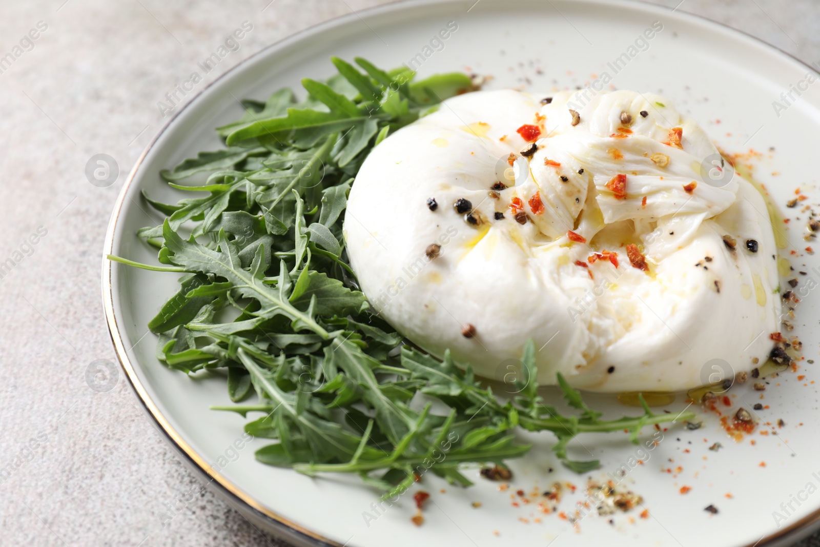 Photo of Delicious burrata cheese, arugula and spices on grey table, closeup