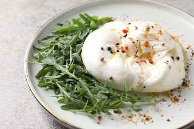 Delicious burrata cheese, arugula and spices on grey table, closeup