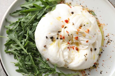 Delicious burrata cheese, arugula and spices on table, top view