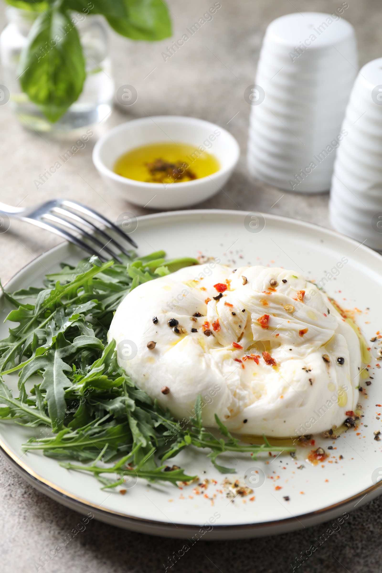 Photo of Delicious burrata cheese, arugula and spices on grey table, closeup