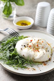 Delicious burrata cheese, arugula and spices on grey table, closeup