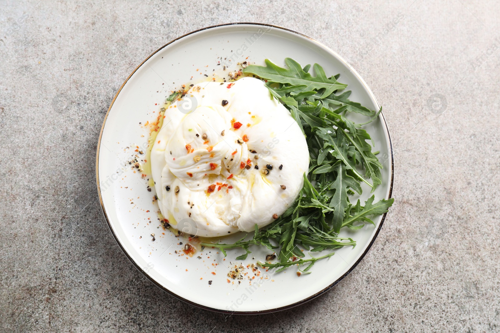 Photo of Delicious burrata cheese, arugula and spices on grey table, top view