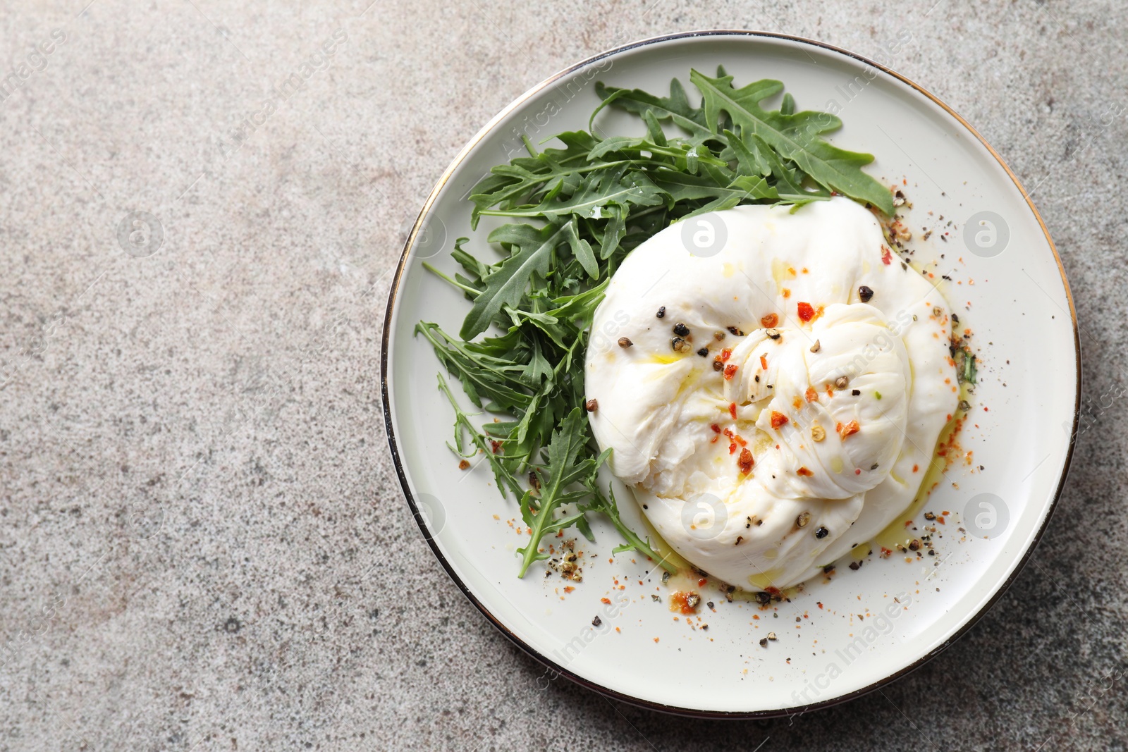 Photo of Delicious burrata cheese, arugula and spices on grey table, top view. Space for text