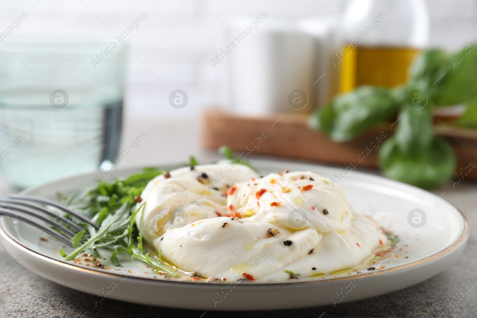 Photo of Delicious burrata cheese, arugula and spices on grey table, closeup