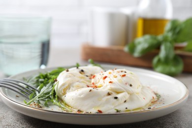 Photo of Delicious burrata cheese, arugula and spices on grey table, closeup