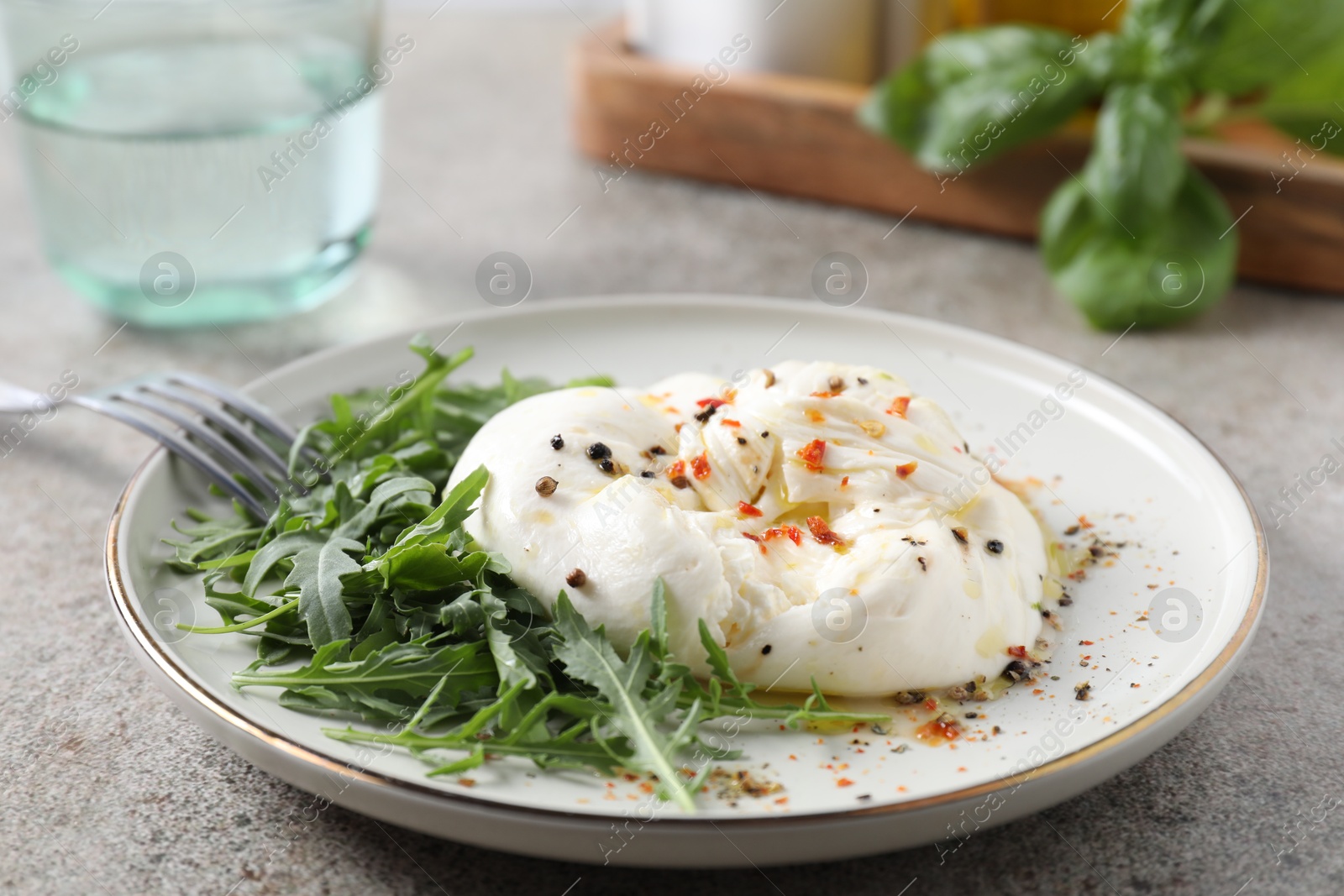 Photo of Delicious burrata cheese, arugula and spices on grey table, closeup