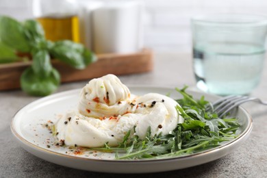 Photo of Delicious burrata cheese, arugula and spices on grey table, closeup