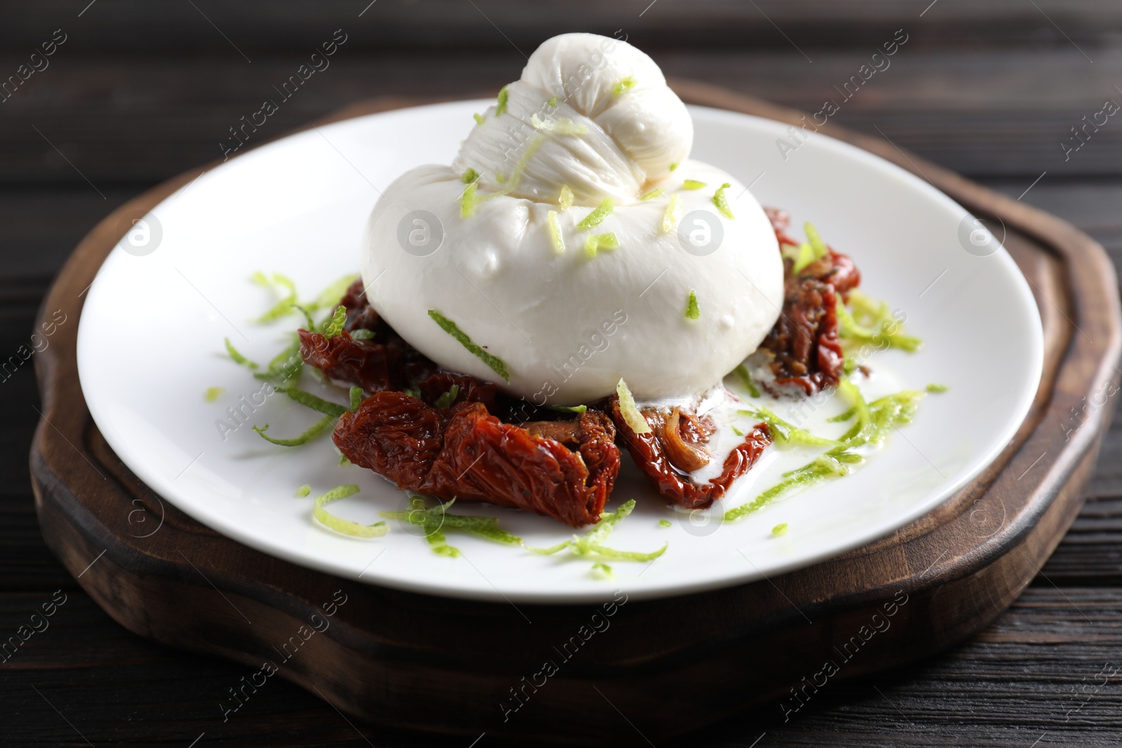 Photo of Delicious burrata cheese and sun-dried tomatoes on wooden table, closeup