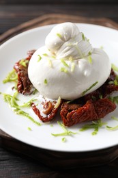 Delicious burrata cheese and sun-dried tomatoes on wooden table, closeup