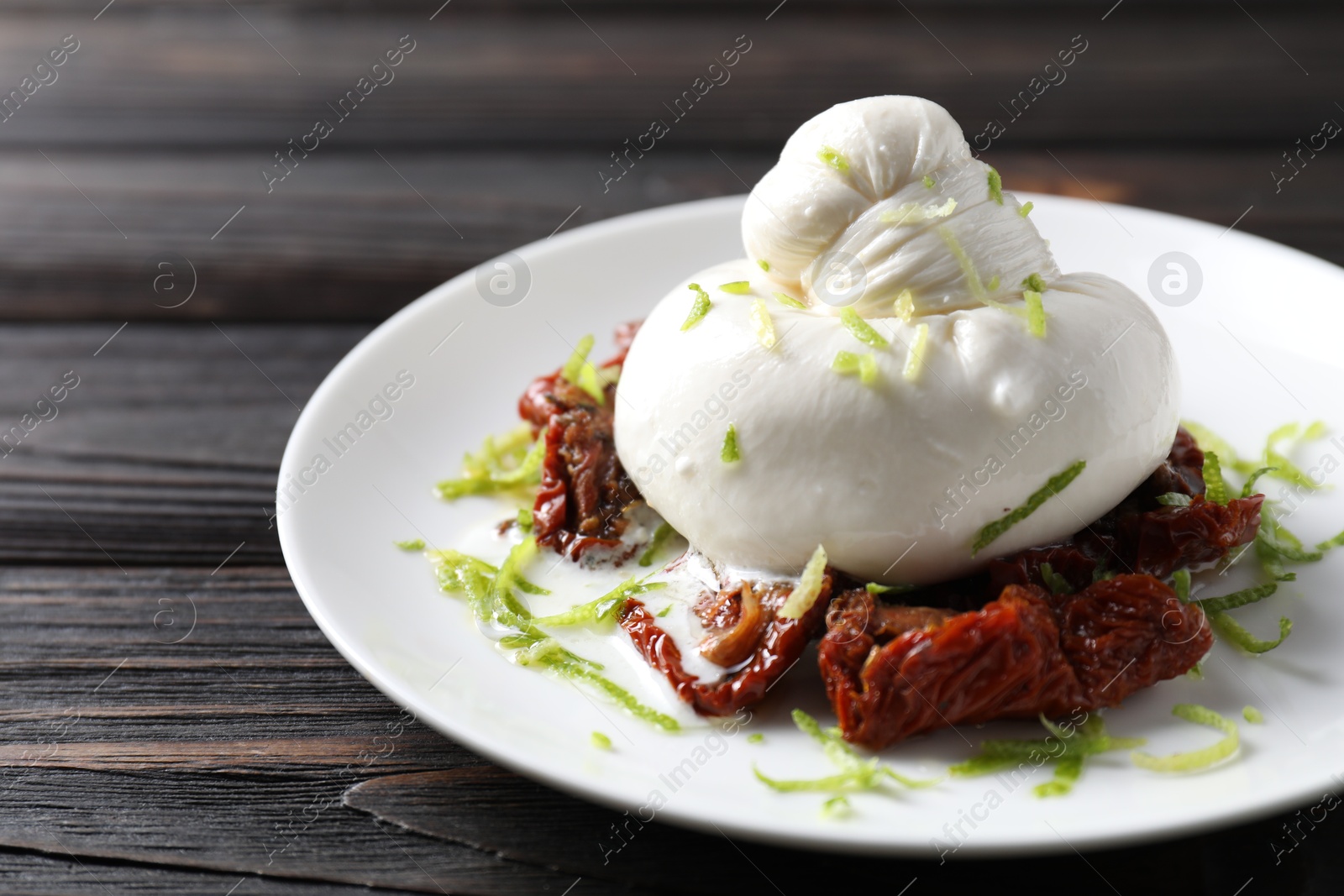 Photo of Delicious burrata cheese and sun-dried tomatoes on wooden table, closeup