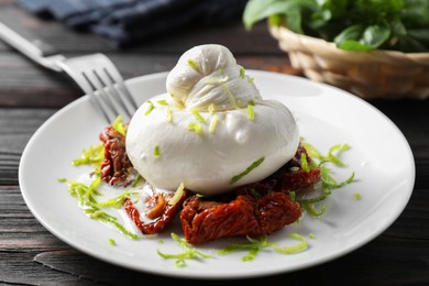 Delicious burrata cheese and sun-dried tomatoes on wooden table, closeup