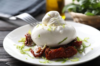 Photo of Delicious burrata cheese and sun-dried tomatoes on wooden table, closeup