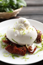 Delicious burrata cheese and sun-dried tomatoes on table, closeup