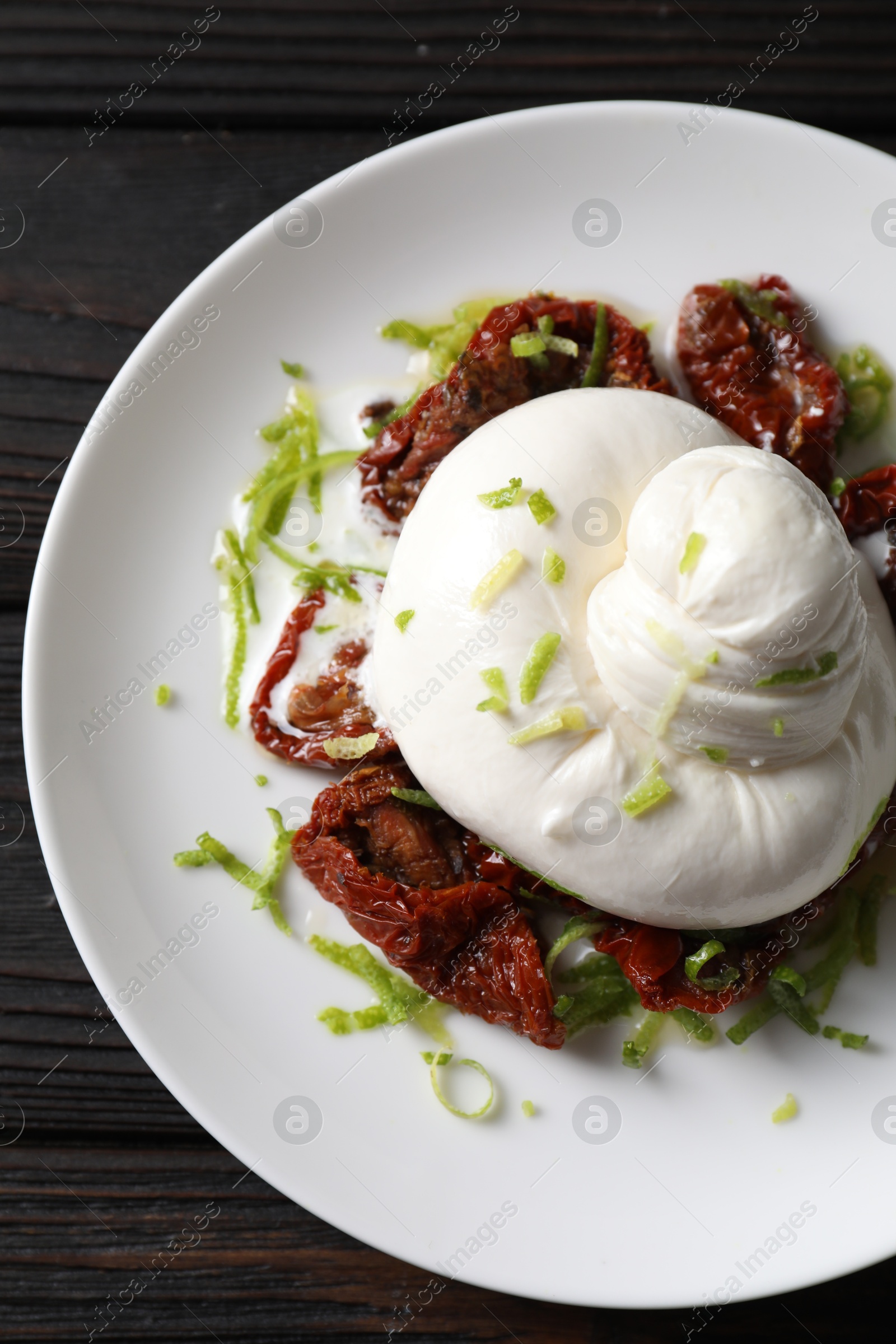 Photo of Delicious burrata cheese and sun-dried tomatoes on wooden table, top view