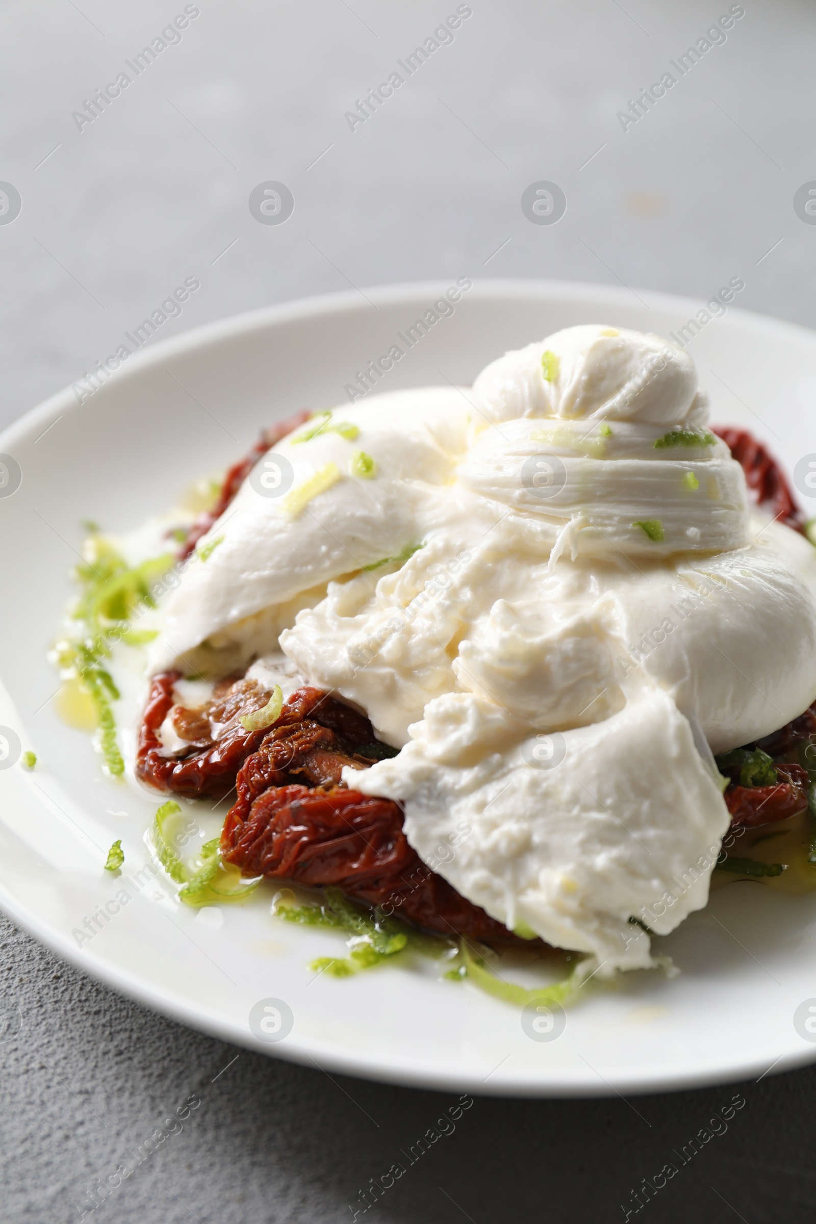 Photo of Delicious burrata cheese and sun-dried tomatoes on light grey table, closeup