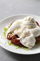 Photo of Delicious burrata cheese and sun-dried tomatoes on light grey table, closeup