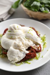 Delicious burrata cheese and sun-dried tomatoes on light grey table, closeup