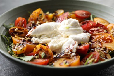 Fresh delicious burrata salad on black table, closeup