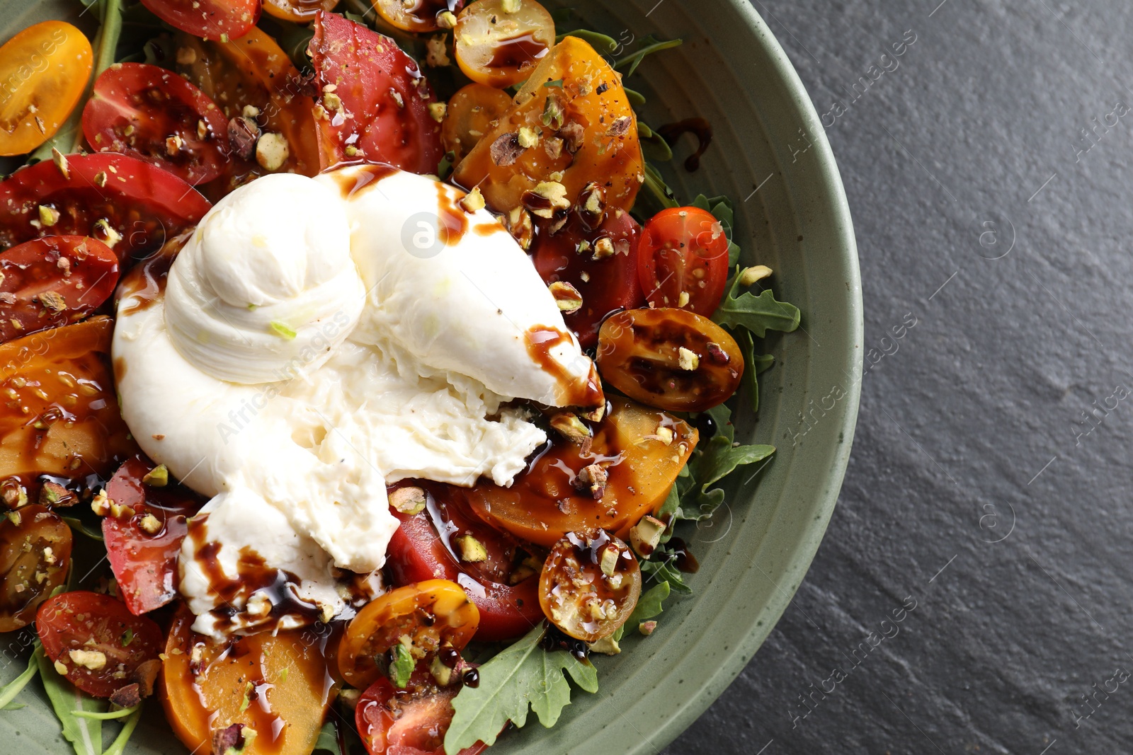 Photo of Fresh delicious burrata salad on black table, top view