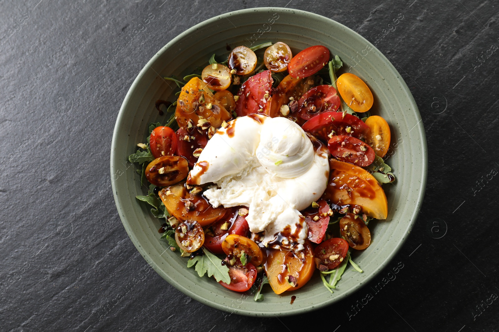 Photo of Fresh delicious burrata salad on black table, top view