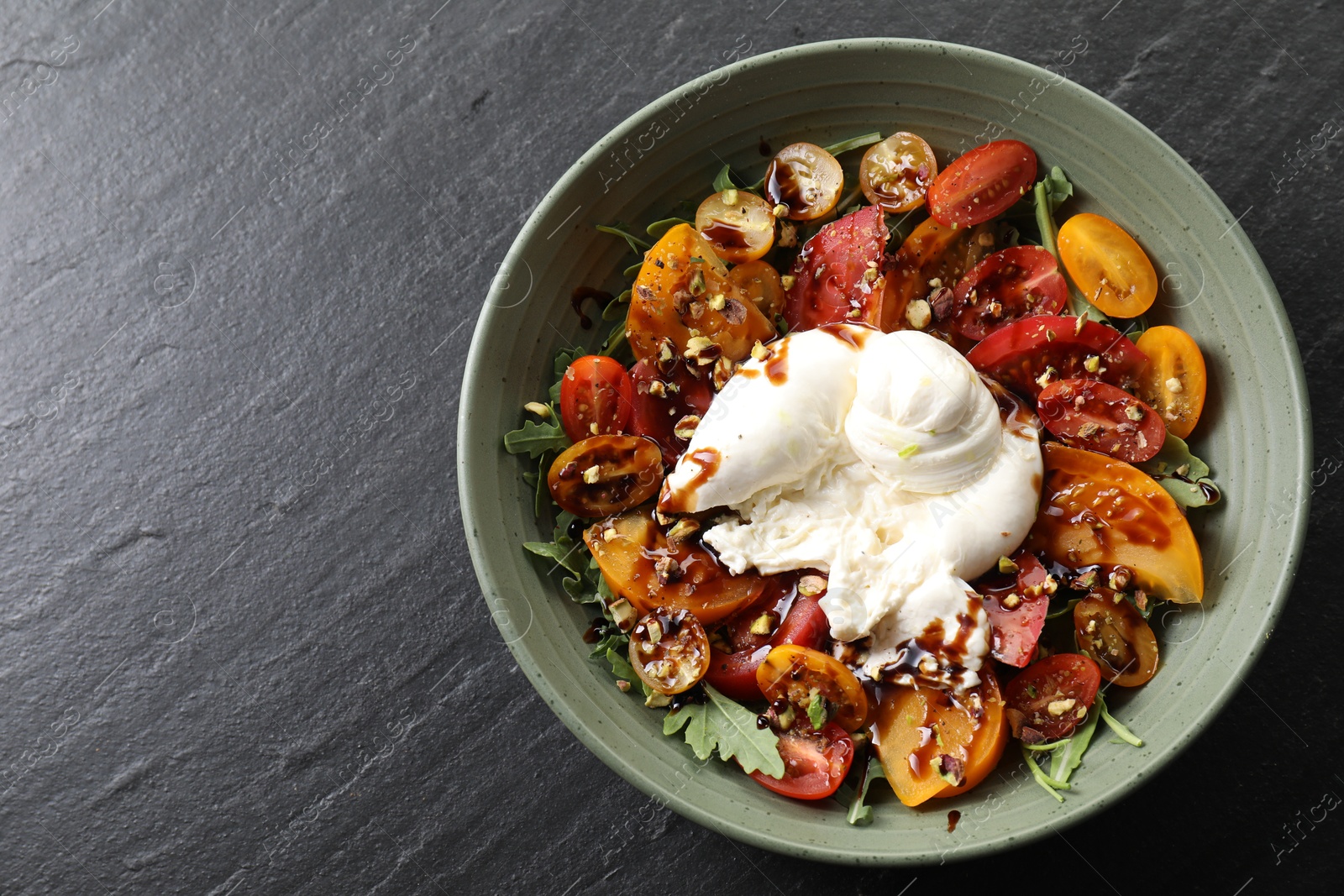 Photo of Fresh delicious burrata salad on black table, top view. Space for text