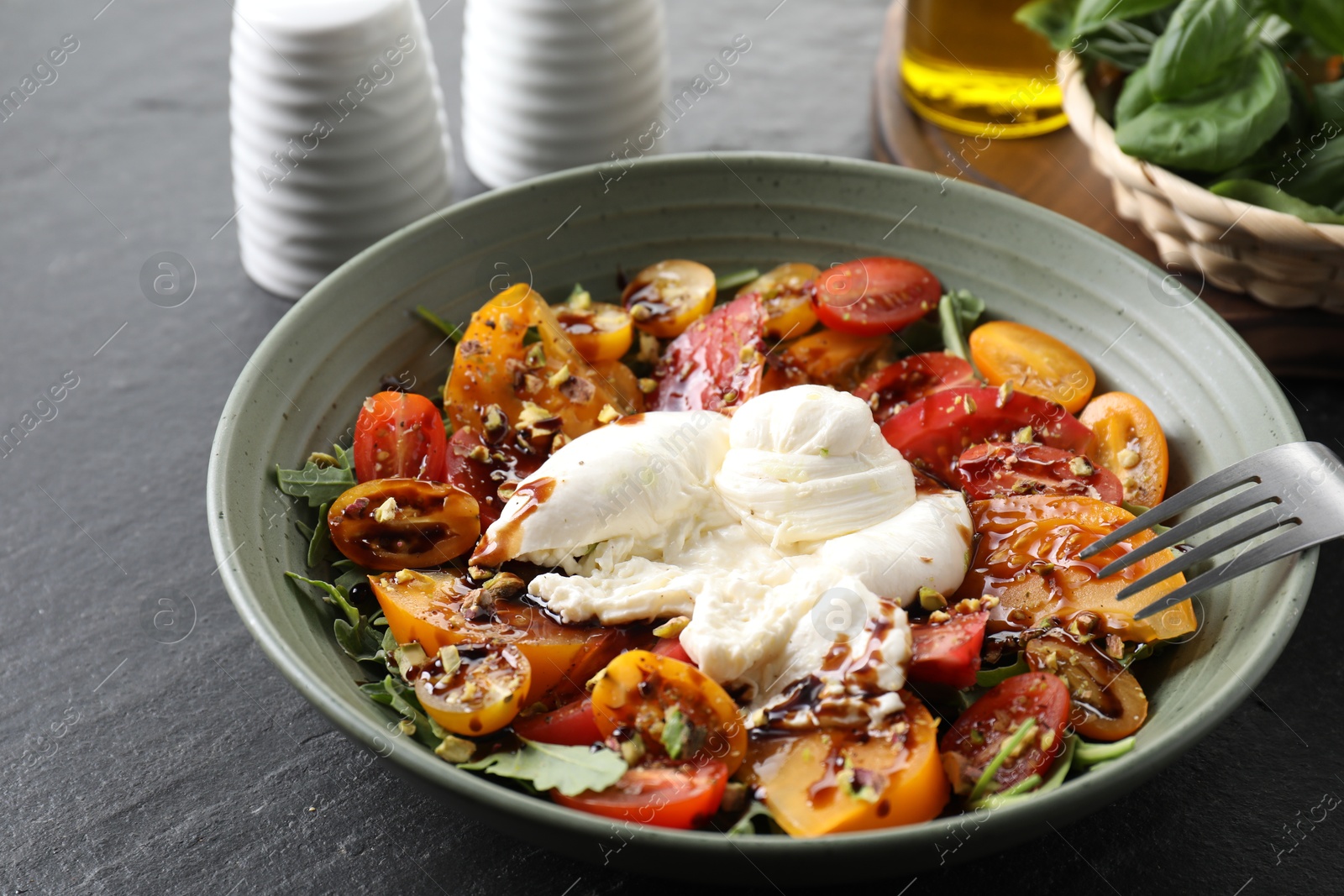 Photo of Fresh delicious burrata salad served on black table, closeup