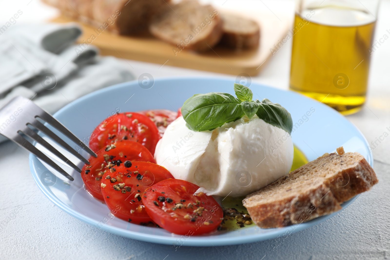 Photo of Delicious burrata cheese, tomatoes, basil and bread on white table, closeup