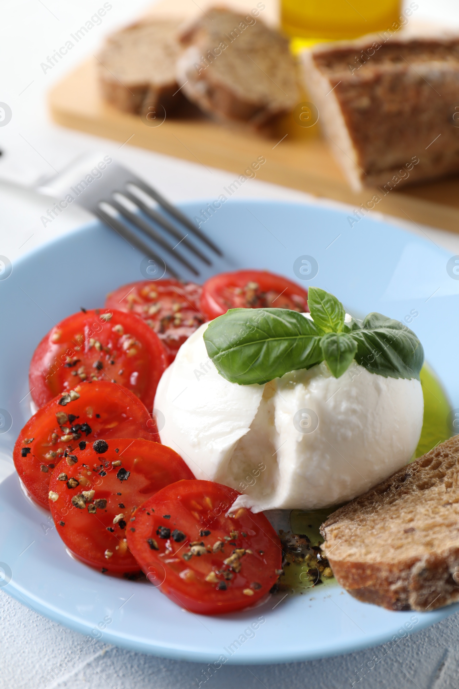 Photo of Delicious burrata cheese, tomatoes, basil and bread on white table, closeup