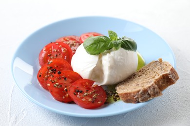 Photo of Delicious burrata cheese, tomatoes, basil and bread on white table, closeup