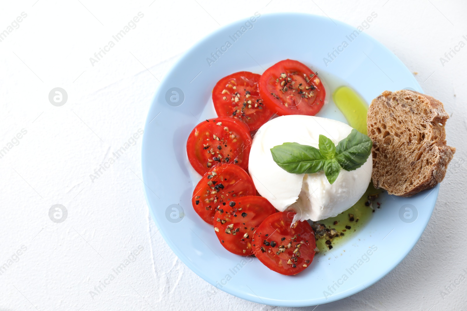 Photo of Delicious burrata cheese, tomatoes, basil and bread on white table, top view. Space for text