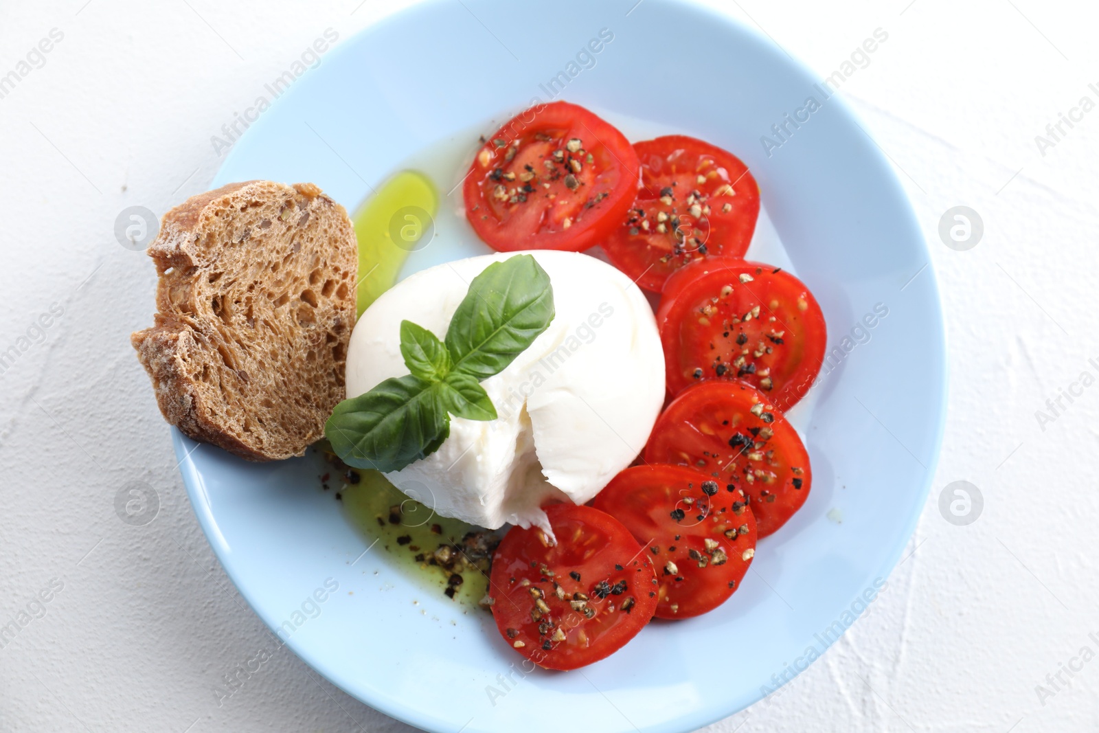 Photo of Delicious burrata cheese, tomatoes, basil and bread on white table, top view