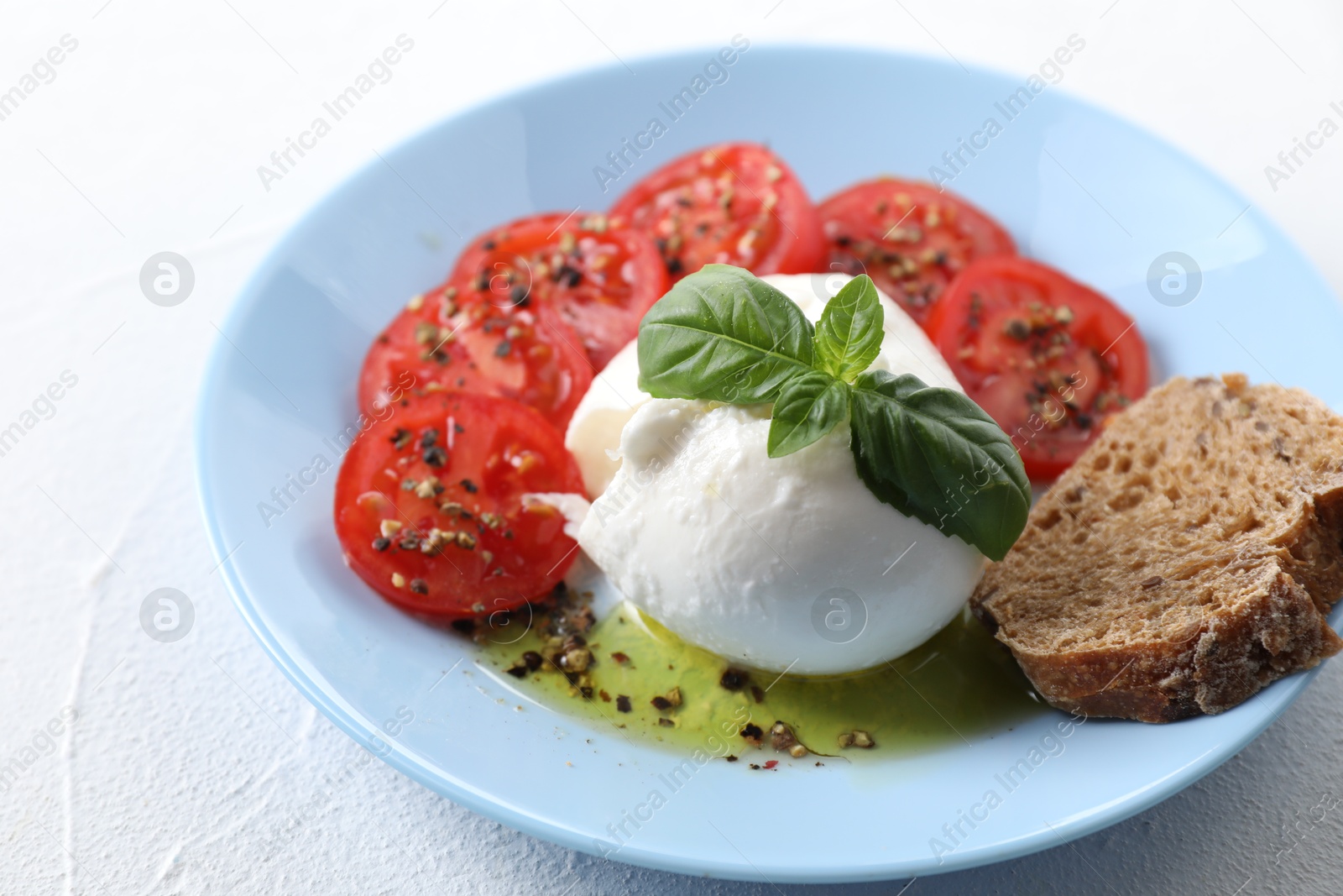 Photo of Delicious burrata cheese, tomatoes, basil and bread on white table, closeup