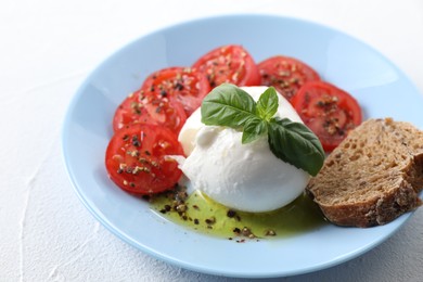 Delicious burrata cheese, tomatoes, basil and bread on white table, closeup