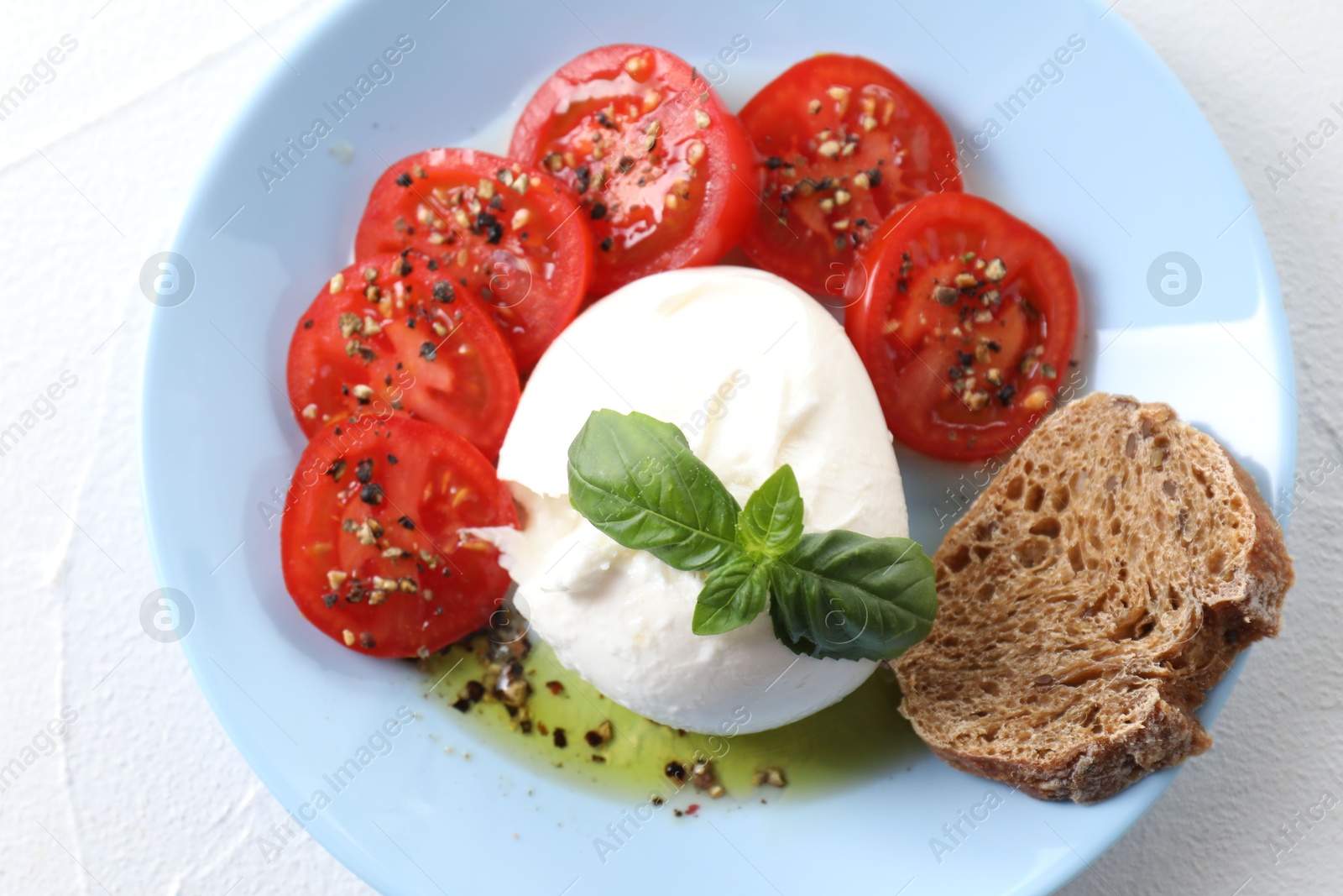 Photo of Delicious burrata cheese, tomatoes, basil and bread on white table, top view