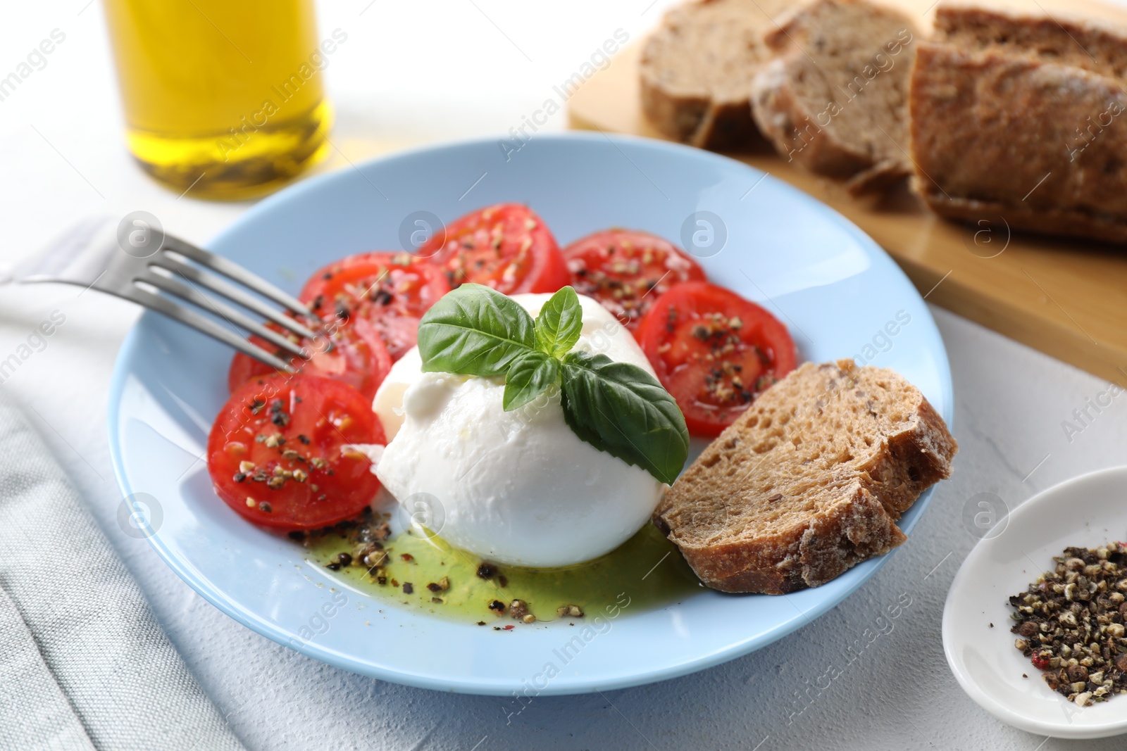 Photo of Delicious burrata cheese, tomatoes, basil, bread and spices on white table, closeup