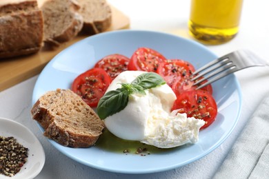 Photo of Delicious burrata cheese, tomatoes, basil, bread and spices on white table, closeup