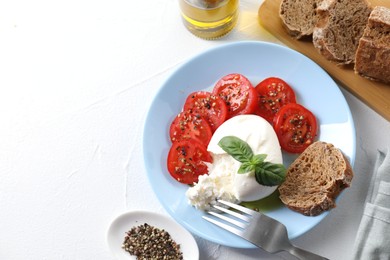 Delicious burrata cheese, tomatoes, basil, bread and spices on white table, top view. Space for text