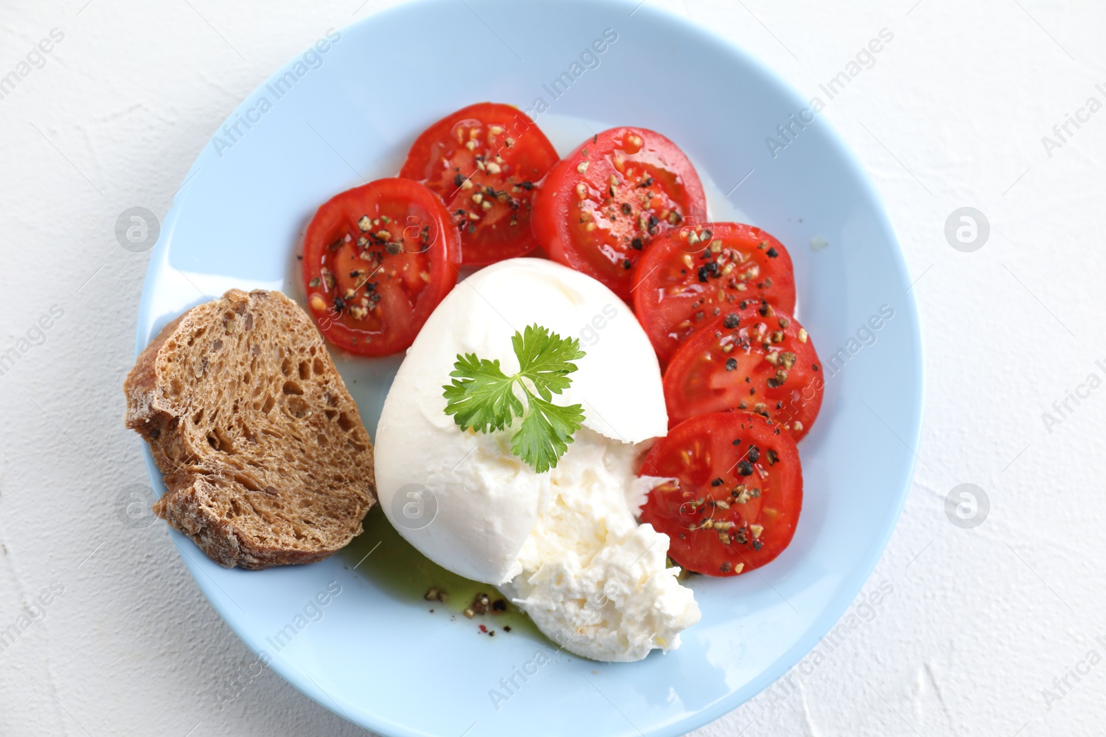 Photo of Delicious burrata cheese, tomatoes, parsley and bread on white table, top view