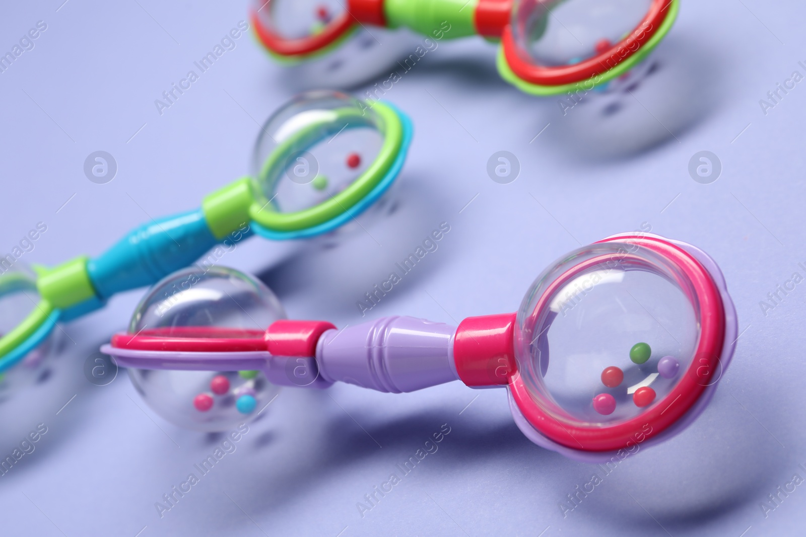 Photo of Colorful rattles on violet background, closeup. Baby accessories