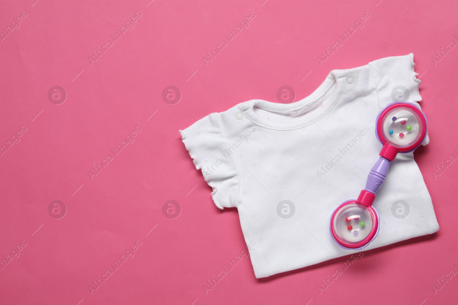 Photo of Colorful rattle and baby shirt on pink background, top view. Space for text