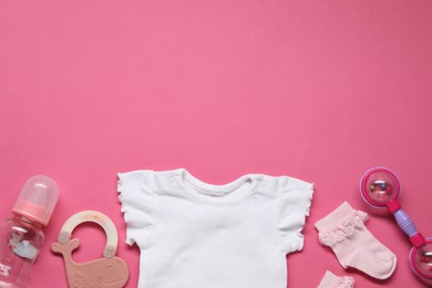 Colorful rattles and baby clothes on pink background, flat lay. Space for text