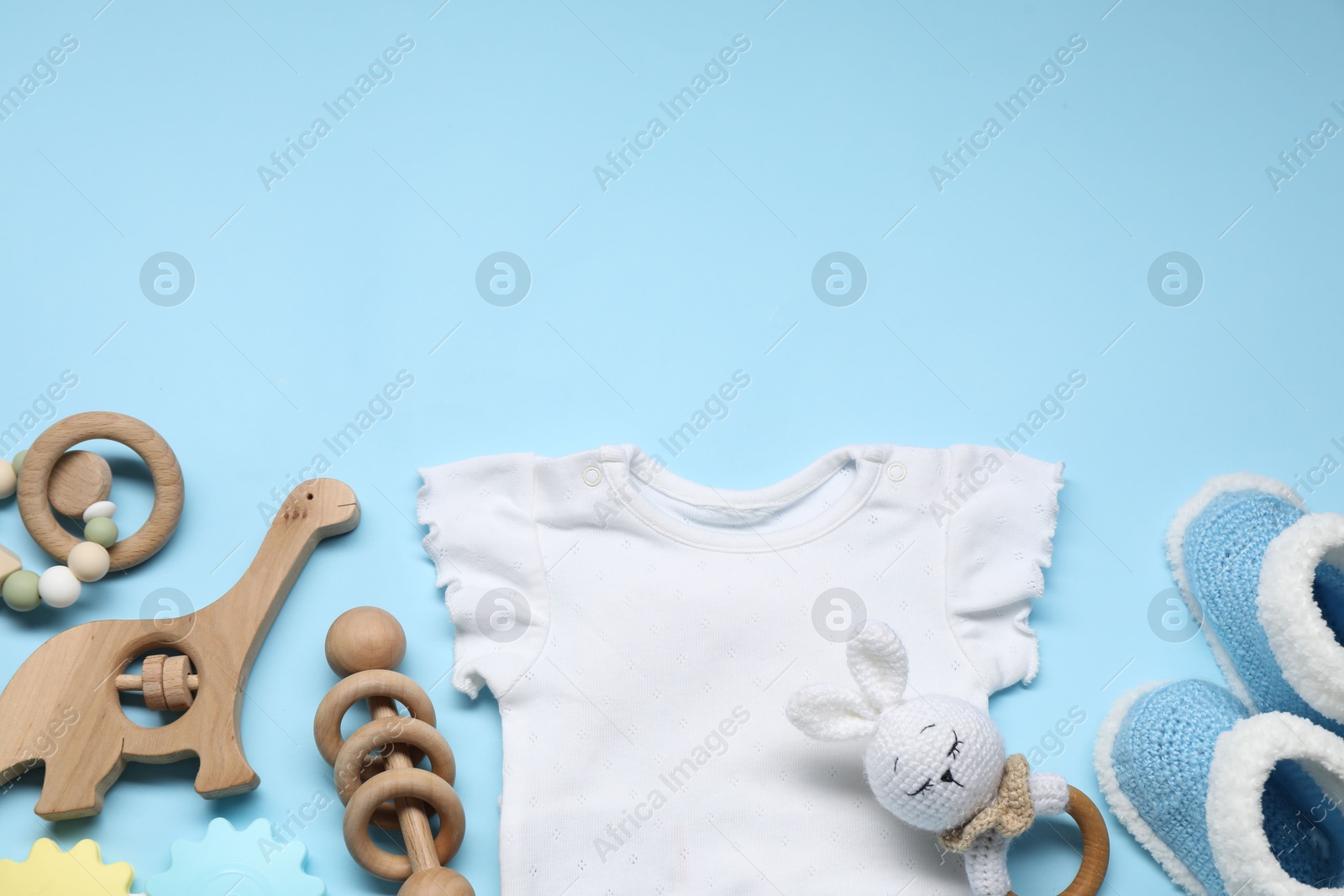 Photo of Wooden rattles, baby shirt and knitted booties on light blue background, flat lay. Space for text