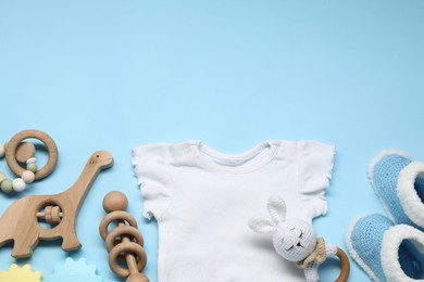 Wooden rattles, baby shirt and knitted booties on light blue background, flat lay. Space for text