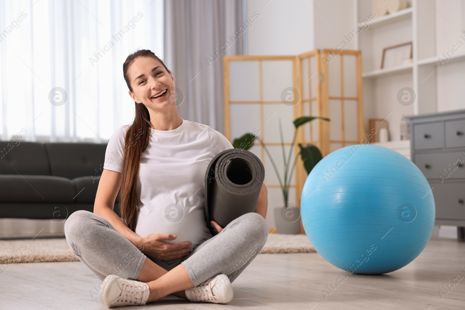 Photo of Smiling pregnant woman with exercise mat and fitball on floor at home