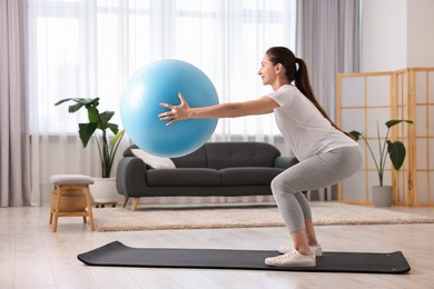 Photo of Beautiful pregnant woman doing exercises with fitball on mat at home