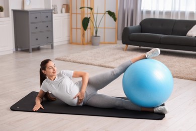 Beautiful pregnant woman doing exercises with fitball on mat at home