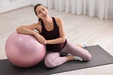 Beautiful pregnant woman with fitball on exercise mat at home