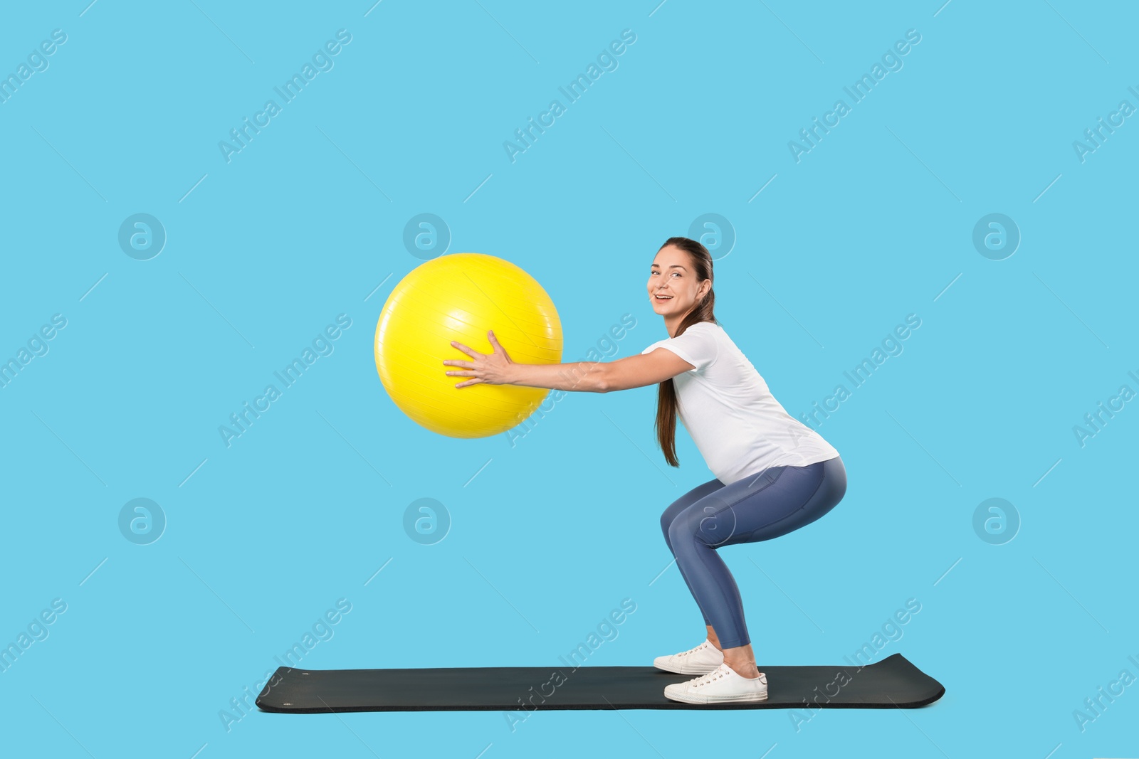 Photo of Beautiful pregnant woman doing exercises with fitball on mat against light blue background