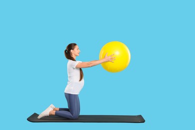 Beautiful pregnant woman doing exercises with fitball on mat against light blue background