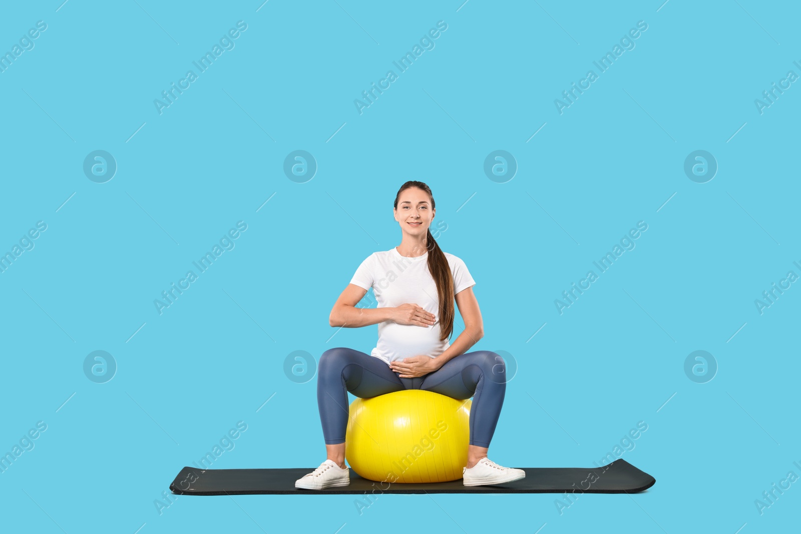 Photo of Beautiful pregnant woman doing exercises on fitball against light blue background